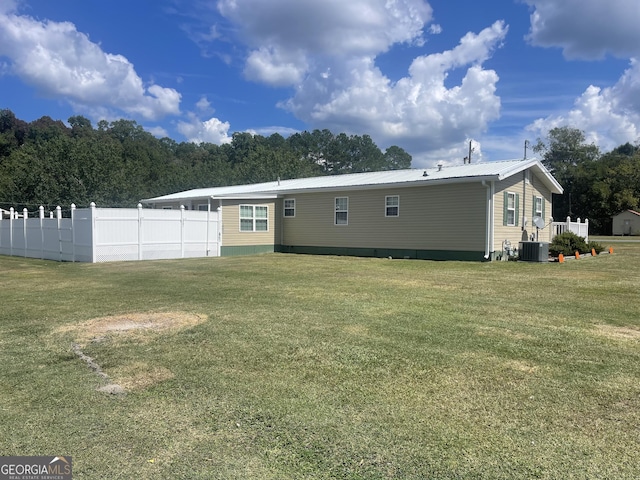 rear view of property featuring central AC unit, fence, a yard, and metal roof