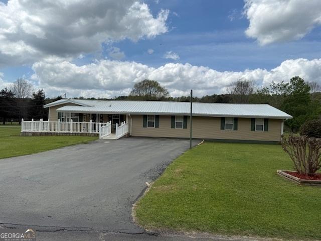 single story home featuring driveway, covered porch, metal roof, and a front yard