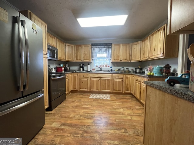 kitchen with dark countertops, light brown cabinets, a sink, light wood-type flooring, and appliances with stainless steel finishes