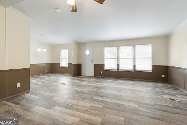 unfurnished living room with wainscoting, wood finished floors, visible vents, and ceiling fan with notable chandelier
