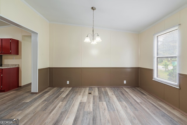 unfurnished dining area with a chandelier, crown molding, a decorative wall, and light wood finished floors