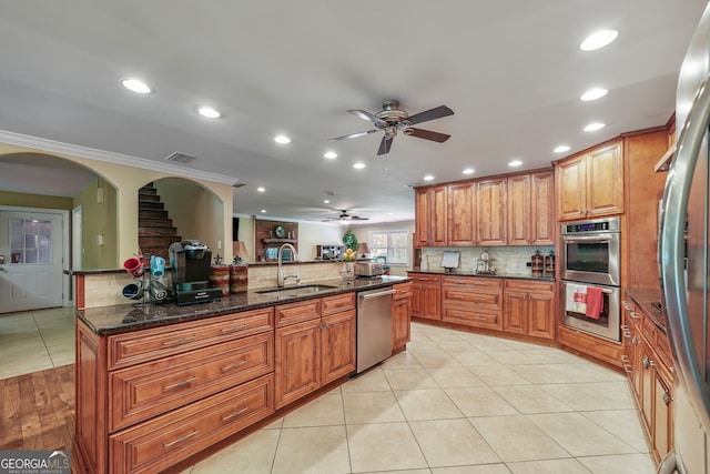 kitchen featuring appliances with stainless steel finishes, a sink, a ceiling fan, brown cabinetry, and tasteful backsplash