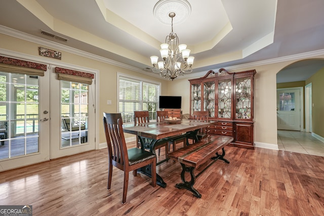 dining area with a chandelier, arched walkways, light wood-type flooring, a raised ceiling, and crown molding