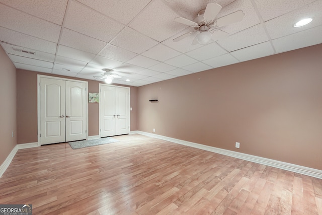 unfurnished bedroom with two closets, light wood-style flooring, baseboards, ceiling fan, and a drop ceiling