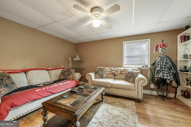 living area with a ceiling fan, a drop ceiling, wood finished floors, and baseboards