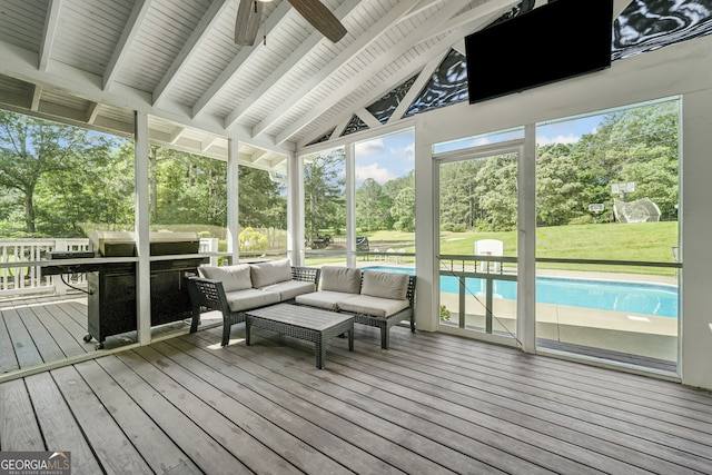 sunroom / solarium with a ceiling fan, an outdoor living space, and view of wooded area