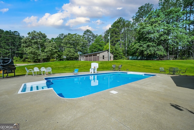 swimming pool with a patio area, a yard, and view of wooded area