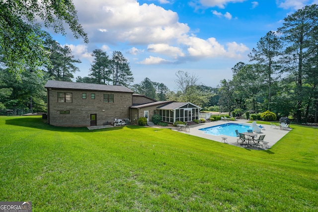 rear view of house featuring a patio area, a sunroom, an outdoor pool, a lawn, and brick siding