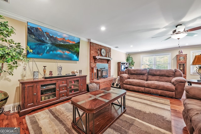 living room with a wood stove, crown molding, wood finished floors, ceiling fan, and recessed lighting
