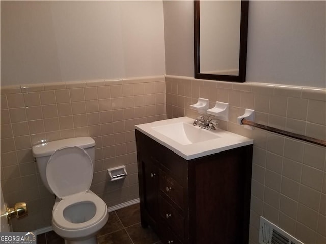 half bath with a wainscoted wall, toilet, tile walls, visible vents, and vanity