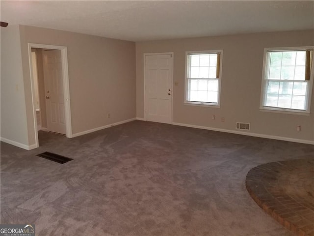 unfurnished living room with baseboards, dark colored carpet, and visible vents