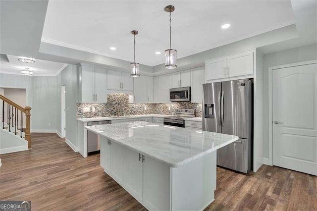 kitchen with tasteful backsplash, stainless steel appliances, a kitchen island, white cabinetry, and a tray ceiling