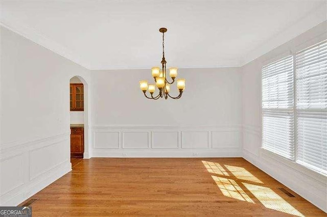 unfurnished dining area featuring a chandelier, a decorative wall, arched walkways, wood finished floors, and wainscoting