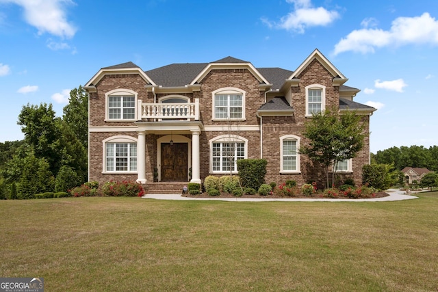 view of front of property featuring brick siding, a balcony, and a front lawn
