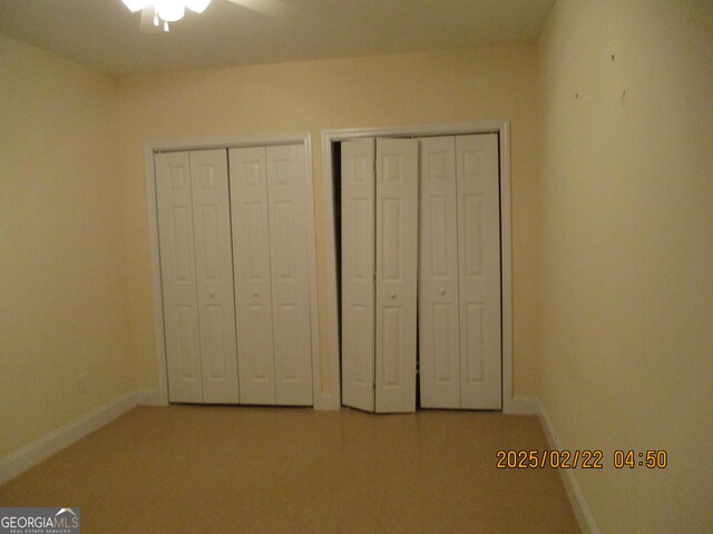 unfurnished bedroom with two closets, baseboards, and a ceiling fan