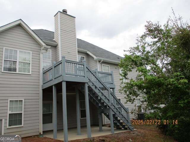 rear view of house with stairway, a chimney, a shingled roof, a patio, and a deck