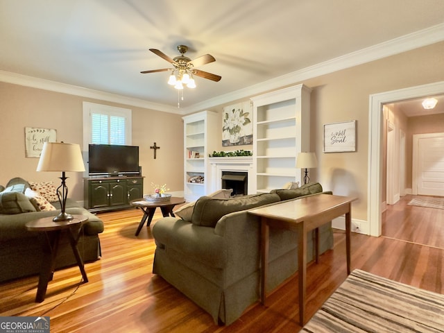 living room with a ceiling fan, crown molding, a fireplace, baseboards, and light wood-style flooring