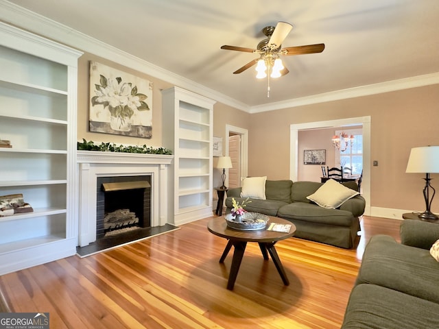 living area with crown molding, ceiling fan, a fireplace, built in shelves, and wood finished floors