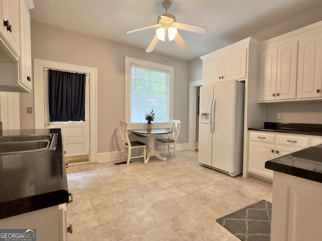 kitchen featuring dark countertops, ceiling fan, white refrigerator with ice dispenser, and white cabinets