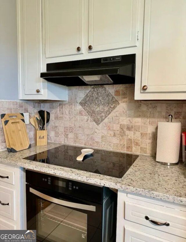 2461 Mcalpin Ter, East Point, GA 30344 - kitchen with under cabinet range hood, black appliances, white cabinetry, and decorative backsplash