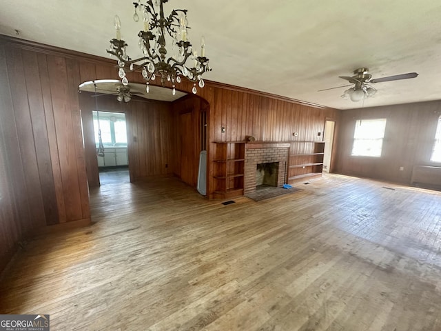 623 Mcdonald St, Waycross, GA 31503 - unfurnished living room featuring a ceiling fan, wooden walls, wood finished floors, arched walkways, and a brick fireplace