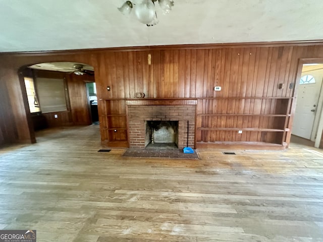623 Mcdonald St, Waycross, GA 31503 - unfurnished living room with wooden walls, a fireplace, a ceiling fan, wood finished floors, and arched walkways