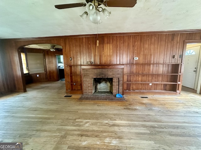 623 Mcdonald St, Waycross, GA 31503 - unfurnished living room with ceiling fan, wooden walls, arched walkways, wood finished floors, and a fireplace