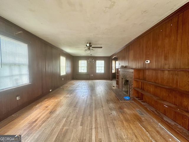 623 Mcdonald St, Waycross, GA 31503 - unfurnished living room with light wood-style floors, a brick fireplace, ceiling fan, wooden walls, and ornamental molding
