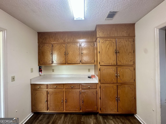 2409 Dorothy St, Waycross, GA 31501 - kitchen featuring dark wood-type flooring, brown cabinetry, a textured ceiling, light countertops, and baseboards