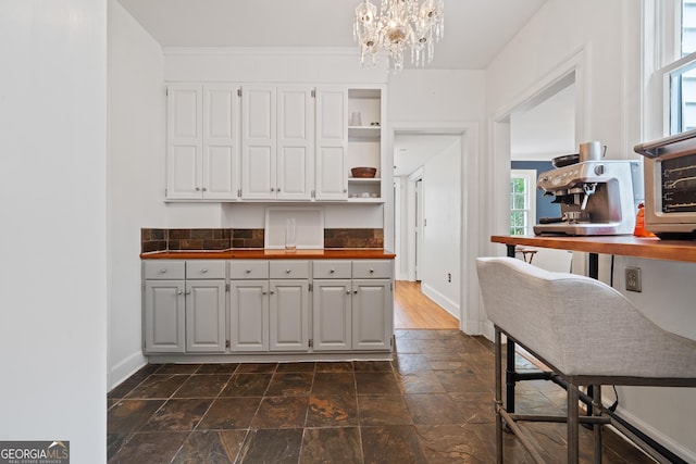 1419 Briarcliff Rd, Macon, GA 31201 - kitchen with dark countertops, open shelves, an inviting chandelier, baseboards, and white cabinetry