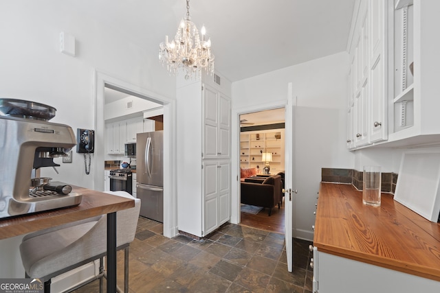 1419 Briarcliff Rd, Macon, GA 31201 - kitchen with white cabinets, freestanding refrigerator, stone finish flooring, gas stove, and a notable chandelier