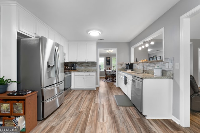 kitchen with backsplash, appliances with stainless steel finishes, a sink, and light wood-type flooring