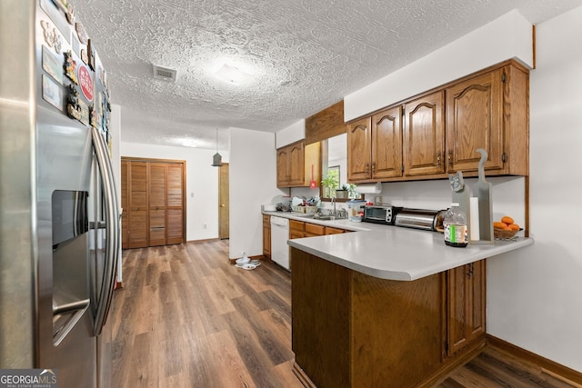 4701 Cleveland Hwy, Gainesville, GA 30506 - kitchen with stainless steel refrigerator with ice dispenser, dishwasher, brown cabinetry, dark wood finished floors, and a peninsula