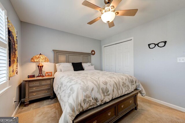 bedroom with light colored carpet, baseboards, a ceiling fan, and a closet