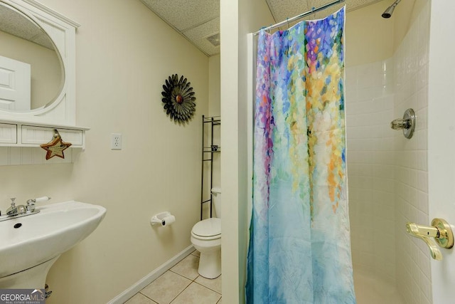 full bath with tiled shower, tile patterned floors, toilet, a sink, and baseboards
