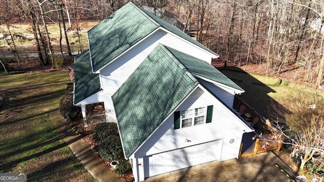 view of side of home with a garage, roof with shingles, and a wooded view