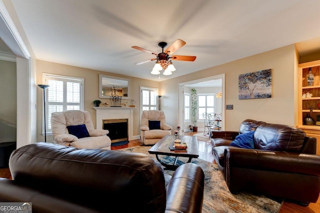 living area with a ceiling fan, a fireplace with flush hearth, and wood finished floors