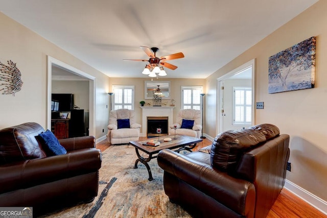 living area featuring a fireplace, a ceiling fan, wood finished floors, and baseboards