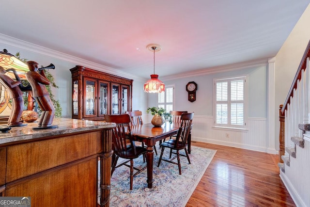 dining room featuring stairway, ornamental molding, a wainscoted wall, and light wood finished floors