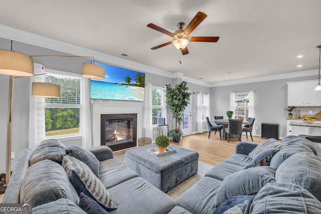 living area featuring crown molding, a glass covered fireplace, a ceiling fan, recessed lighting, and light wood-type flooring