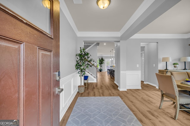 entrance foyer with a decorative wall, ornamental molding, a wainscoted wall, and light wood-type flooring