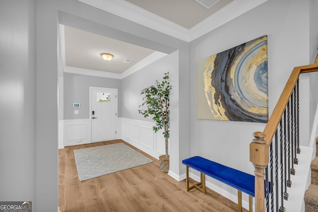 foyer featuring crown molding, a wainscoted wall, visible vents, and wood finished floors