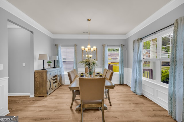 dining room featuring ornamental molding, wainscoting, light wood-type flooring, and a chandelier