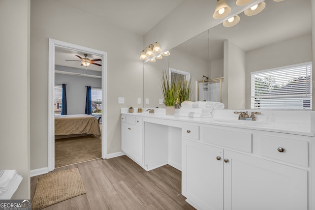 ensuite bathroom with ceiling fan, a sink, double vanity, a shower stall, and wood finished floors