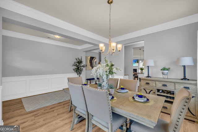 dining room featuring crown molding, light wood-style flooring, wainscoting, and a chandelier