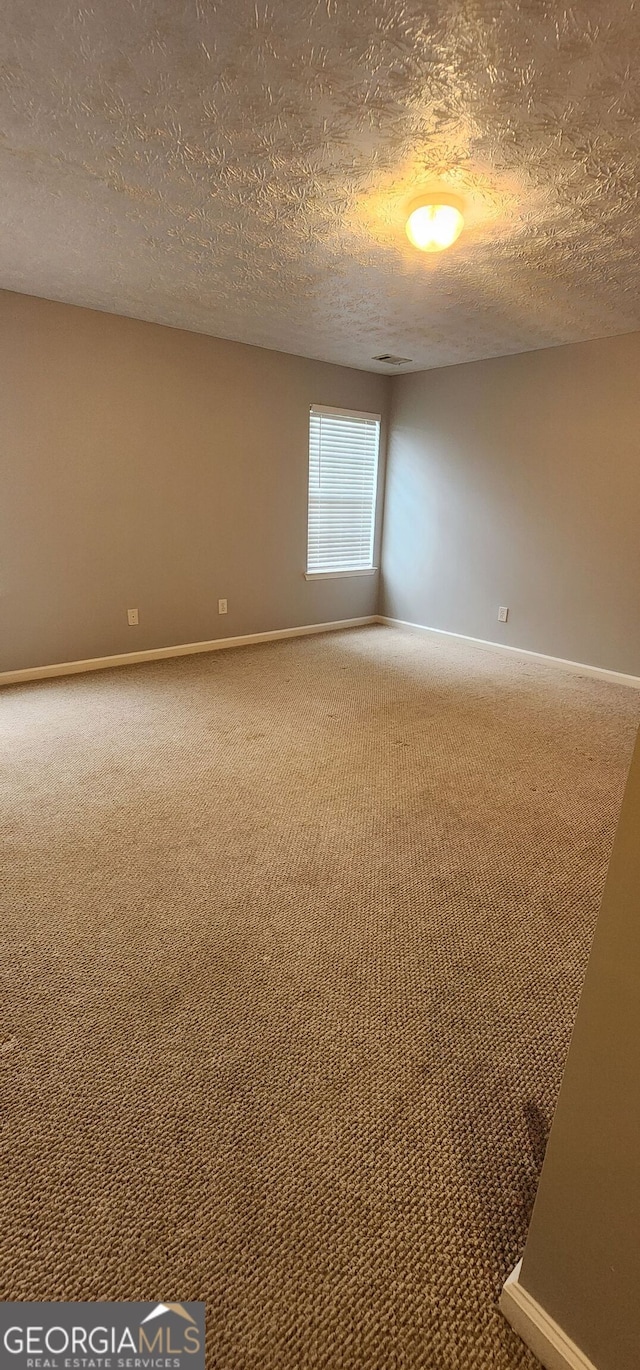 empty room with carpet floors, a textured ceiling, and baseboards