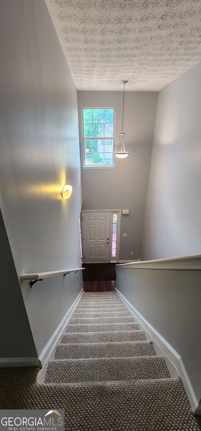 staircase featuring baseboards, a textured ceiling, and carpet