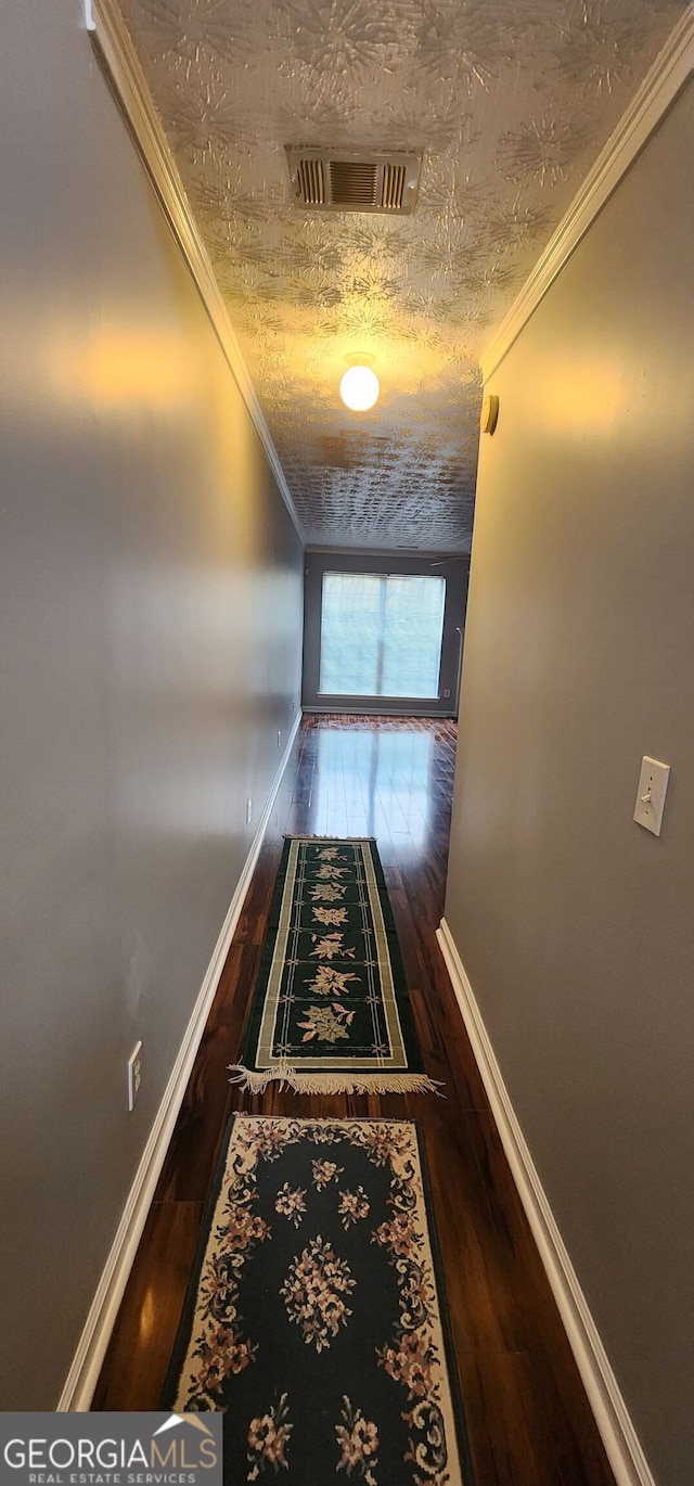 corridor with a textured ceiling, ornamental molding, wood finished floors, and visible vents