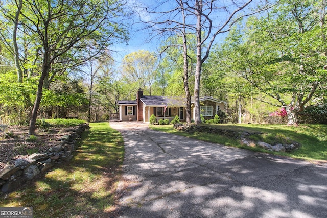 view of front of house featuring a chimney, aphalt driveway, and a front yard