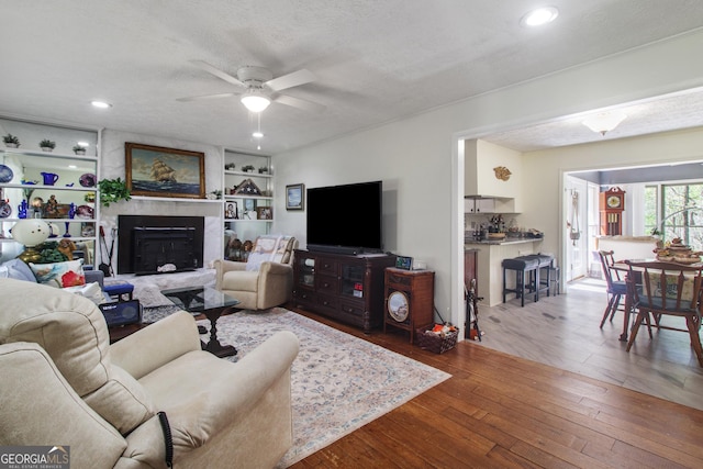 living area featuring a ceiling fan, hardwood / wood-style floors, a textured ceiling, a fireplace, and recessed lighting